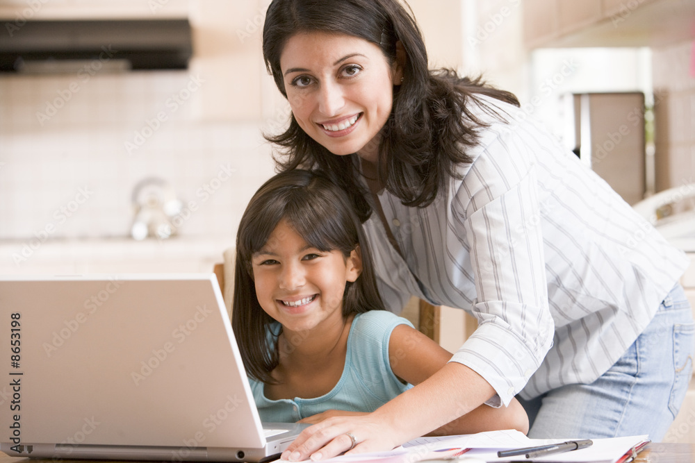 Woman and young girl in kitchen with laptop and paperwork smilin