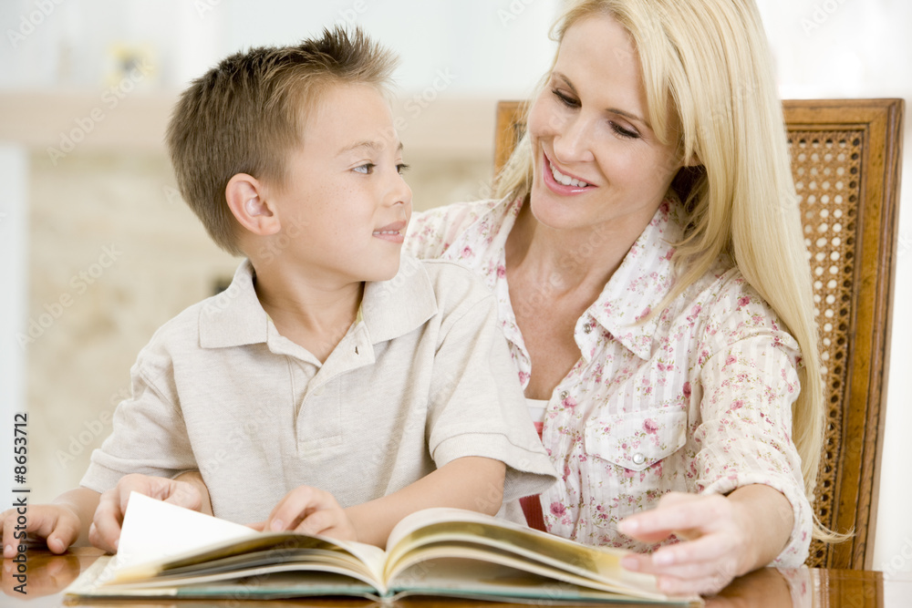 Obraz premium Woman and young boy reading book in dining room smiling