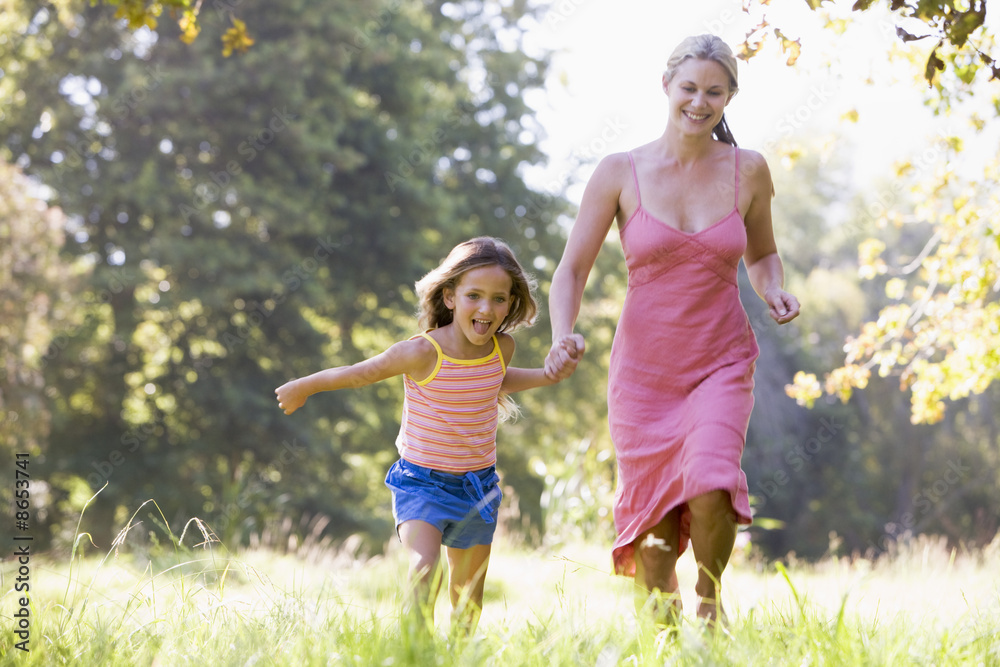 Woman and young girl running outdoors holding hands and smiling Woman and young girl running outdoors holding hands and smiling