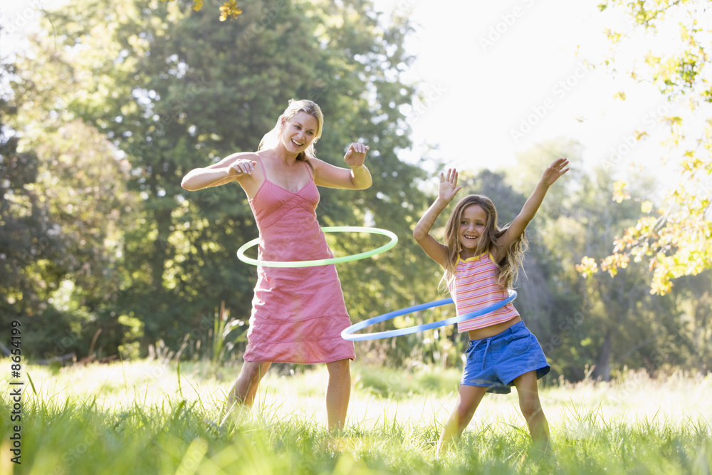Naklejka premium Woman and young girl outdoors using hula hoops and smiling