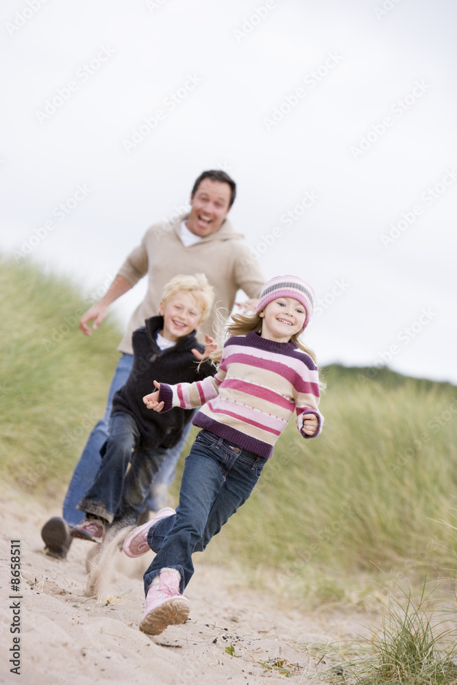 Father and two young children running at beach smiling Father and two young children running at beach smiling