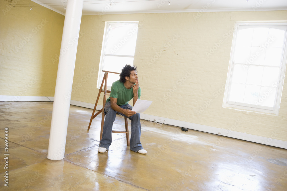 Man sitting on ladder in empty space holding paper thinking Man sitting on ladder in empty space holding paper thinking