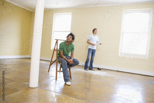 Two men with ladder in empty space holding paper and thinking