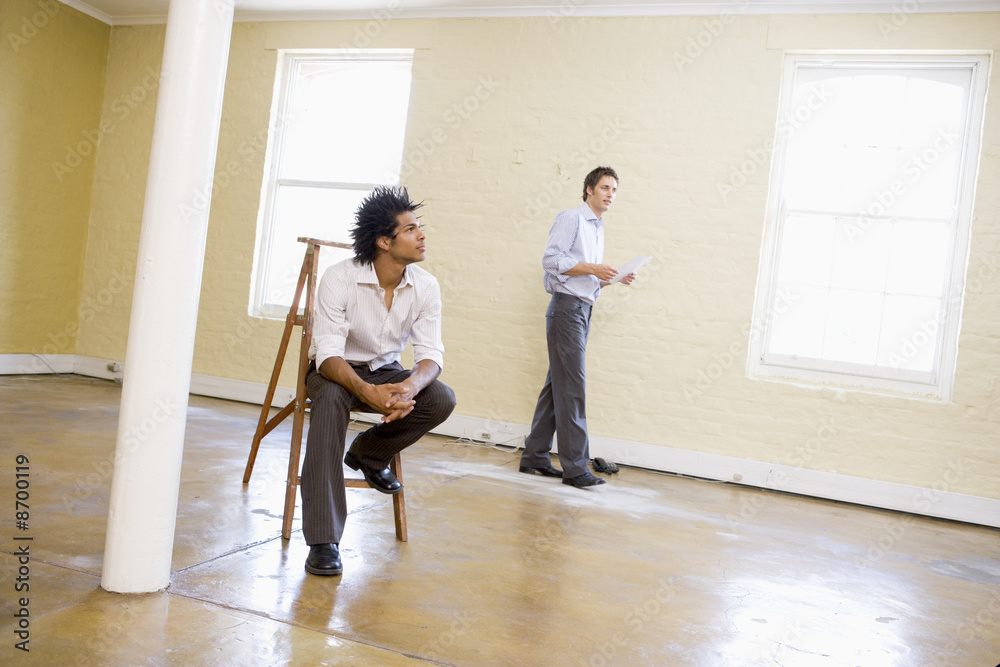 Man sitting on ladder in empty space with other man Man sitting on ladder in empty space with other man
