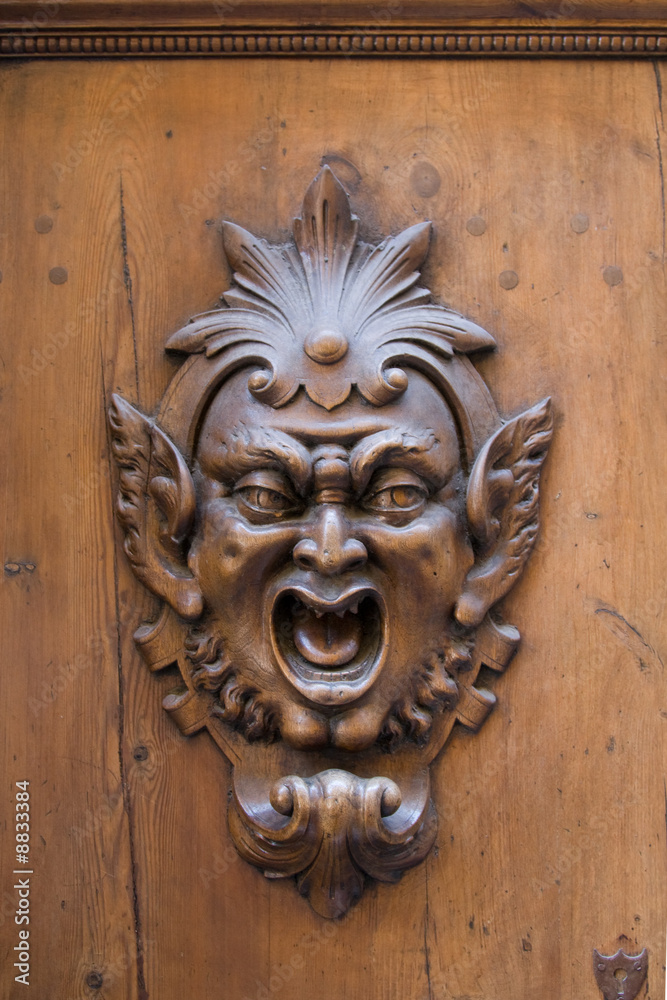 Carved gargoyle adorning a wooden door in Siena, Italy