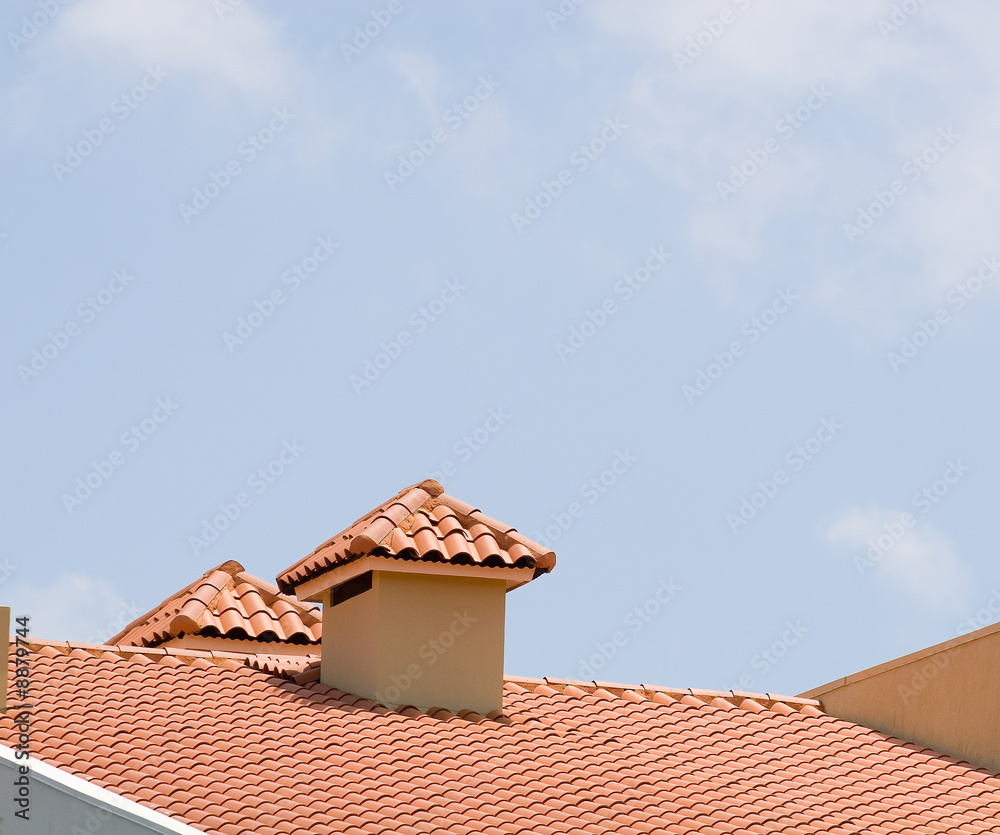 A red tile roof and dormer against a bright blue sky
