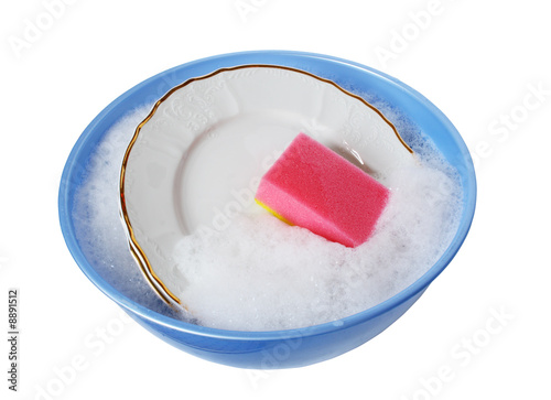 Plates and sponge lying in wash-basin with water and foam