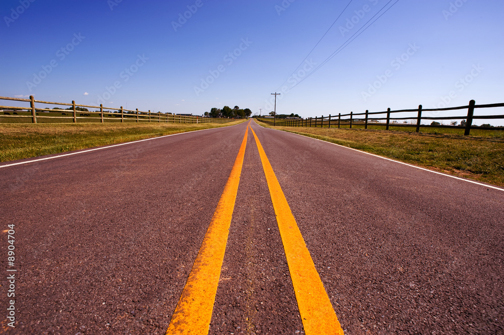 Fototapeta premium A long road bordered by farm fences