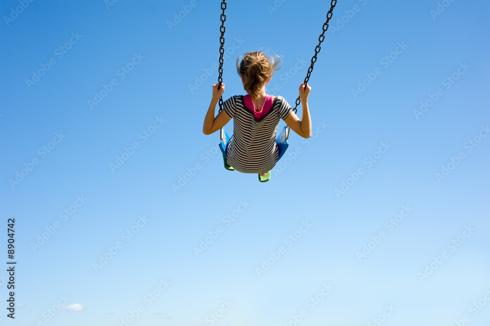 Fototapeta premium A young girl playing on a swingset in front of a blue sky