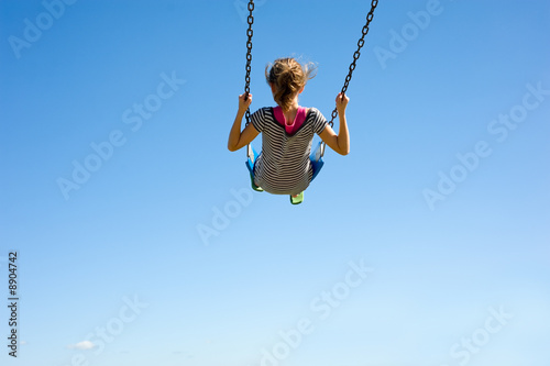 A young girl playing on a swingset in front of a blue sky