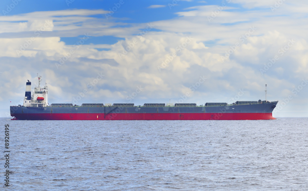 Cargo ship in open sea under cloudy blue sky