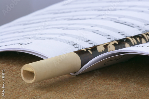 Wooden flute laying on opened book with music sheets