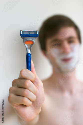 Young caucasian men holding a razor in front of unfocused face