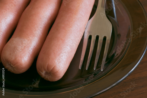 Three sausages with fork on glass plate on table