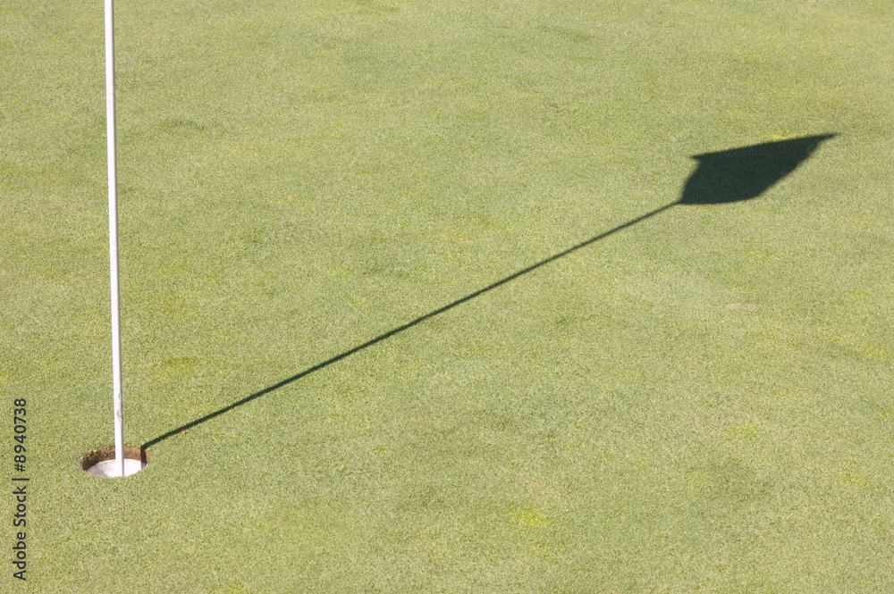 Hole and shadow of a golf green flag on the green