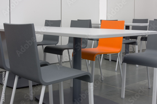 Orangefarbener Stuhl unter grauen Stühlen und Tischen
