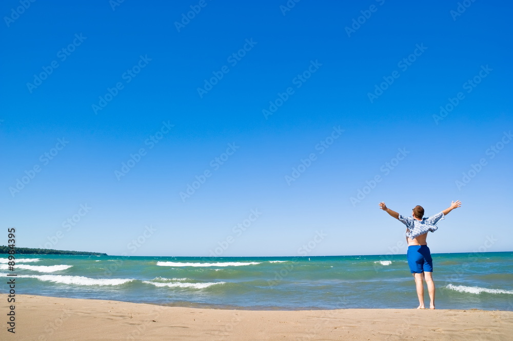 Man with arms outstretched standing on the lakeshore Man with arms outstretched standing on the lakeshore