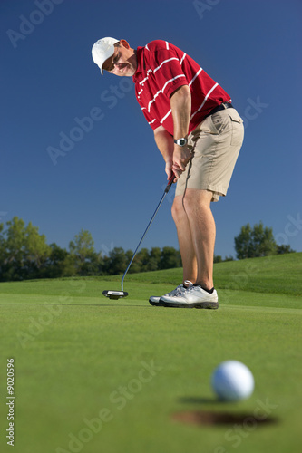 golfball at hole with putting golf player in the back photo