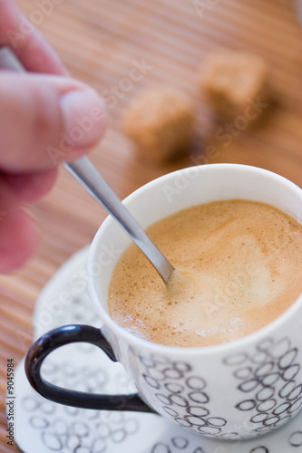 Hand holding a spoon in a cup of coffee with brown sugar