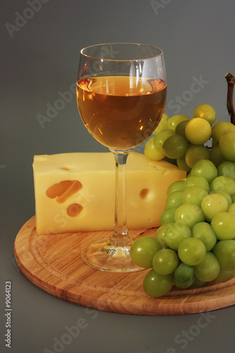 Glass of wine, cheese and grapes on a wooden board