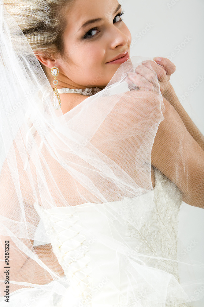 Beautiful bride staring over shoulder at camera holding veil Beautiful bride staring over shoulder at camera holding veil