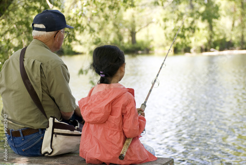 A young girl is fishing with her grandpa on a warm summer day.