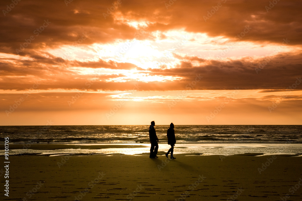 couple walking on the beach with beautiful sunset and waves