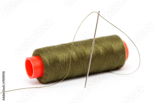 Spool of olive green thread and needle on white background.
