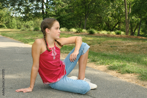Young girl relaxing, sitting on a path in a park