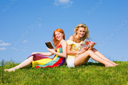 Two girls with notebook outdoors. Sitting on green grass