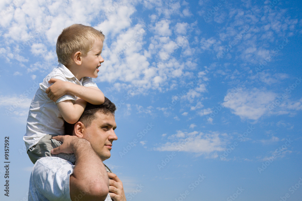Little son sits on father`s shoulders outdoors - obrazy, fototapety, plakaty 