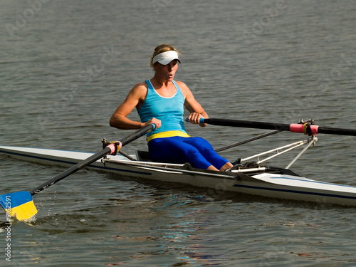 Sporty young lady rowing in boat on water