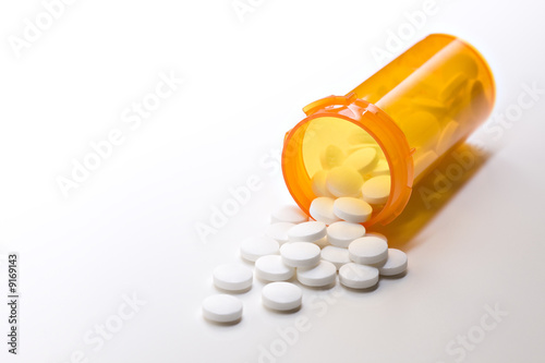 aspirin pills spilling from medicine bottle closeup on white
