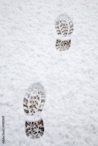 Two footprints in the snow on a wooden deck.
