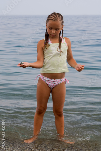 little girl stands in water ashore
