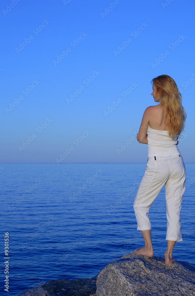 Calm young woman standing on the rock, looking at the sea.
