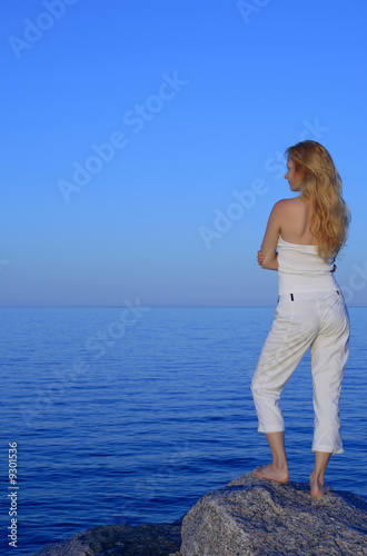 Calm young woman standing on the rock, looking at the sea.