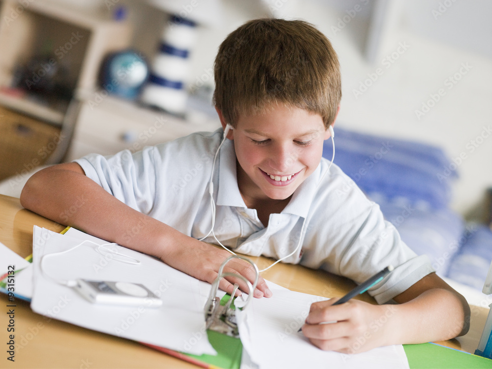 Naklejka premium Young Boy Doing His Homework While Listening To Music On MP3