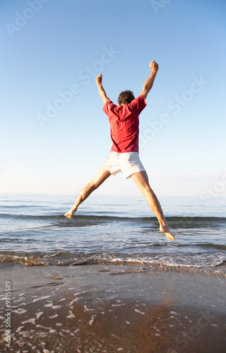 Fototapeta Naklejka Na Ścianę i Meble -  Back view of young man jumping on the beach