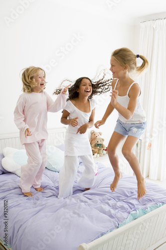 Three Young Girls Jumping On A Bed In Their Pajamas