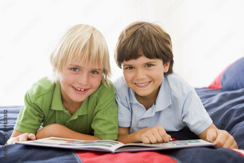Two Young Boys Lying Down On A Bed Reading A Book Two Young Boys Lying Down On A Bed Reading A Book