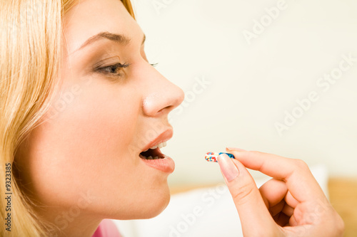 Profile of young woman holding pill by her mouth