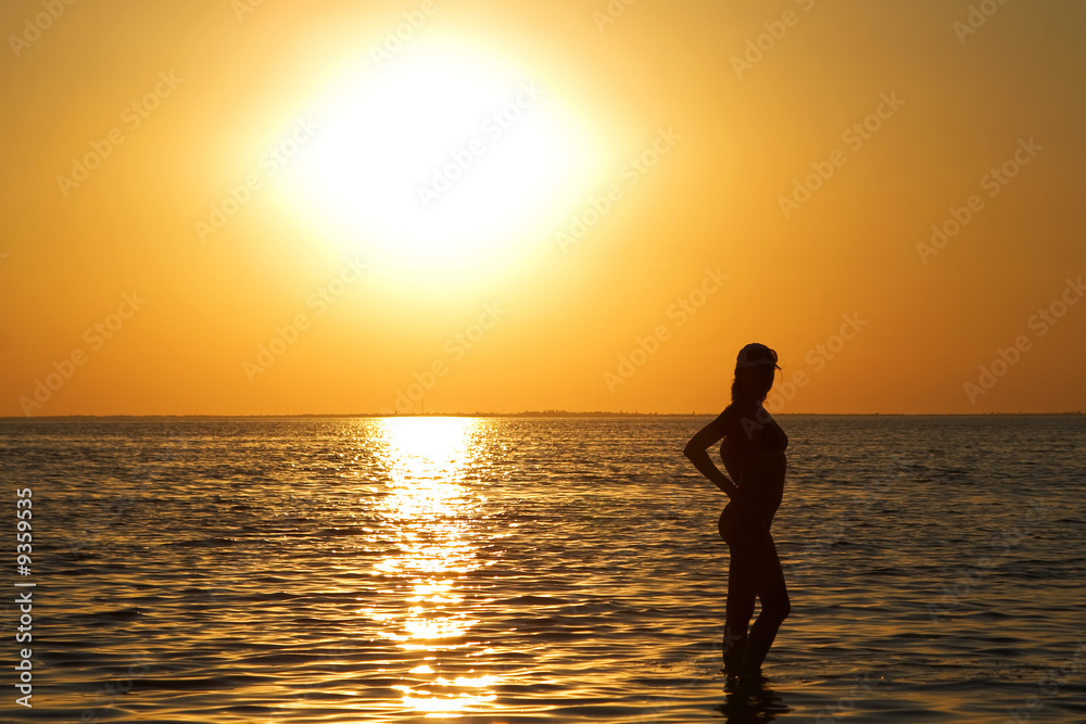 Fototapeta premium Silhouette of the young woman on a sea bay on a sunset