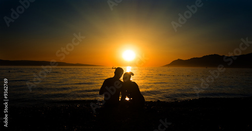 young couple sitting on the beach at the sunset