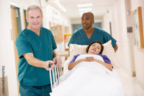 Two Orderlies Pushing A Woman In A Bed Down A Hospital Corridor
