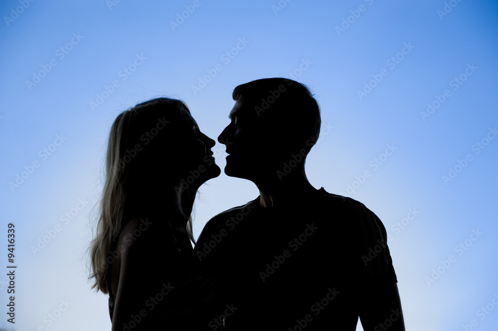 Silhouette of a young couple kissing on blue sky