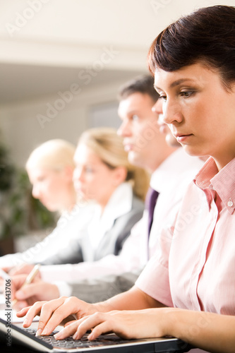 Woman typing on laptop on background of her colleagues