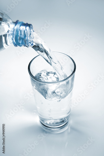 Glass of water being filled from a plastic bottle