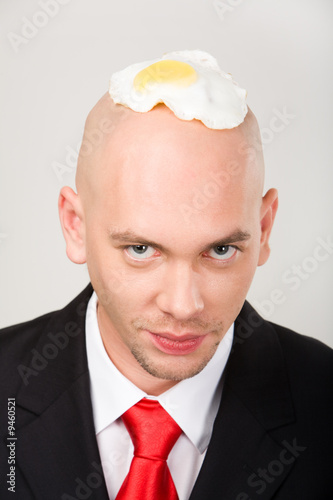Slika na platnu Bald man with fried eggs on top of head looking at camera