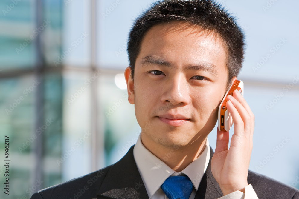 Good looking asian business man standing with mobile phone.